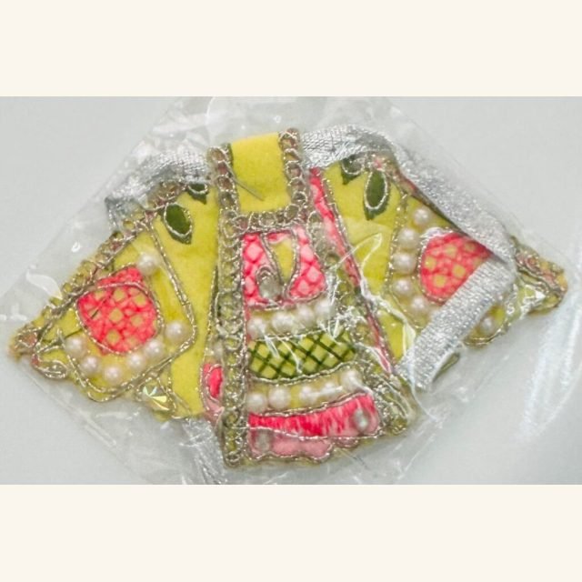Yellow Radha Rani dress with pink and green floral embroidery, pearl decorations, and silver lace, sealed in transparent packaging.