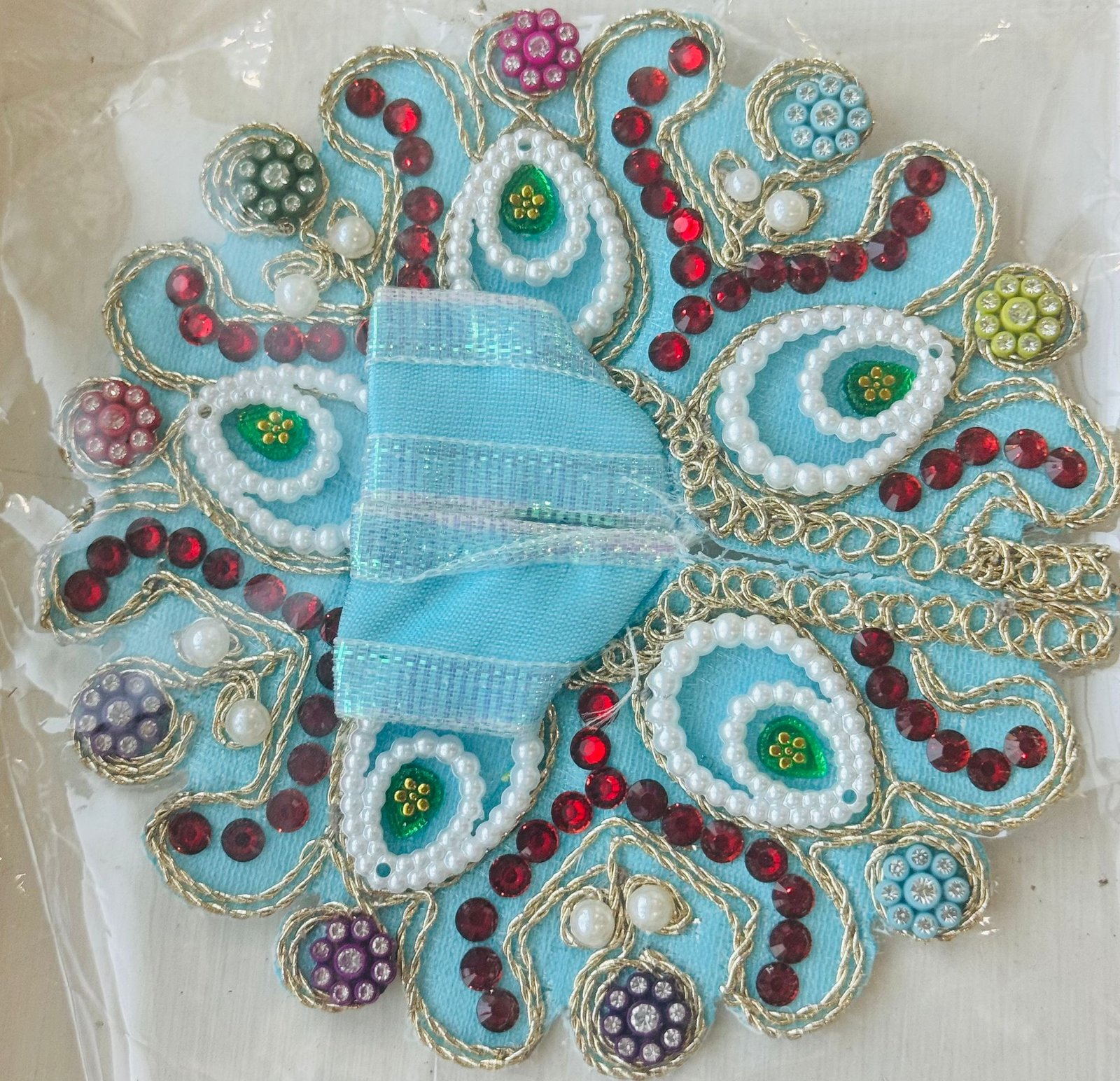 Sky blue Laddu Gopal dress with pearl-lined paisley design, red stones, and multicolor bead accents