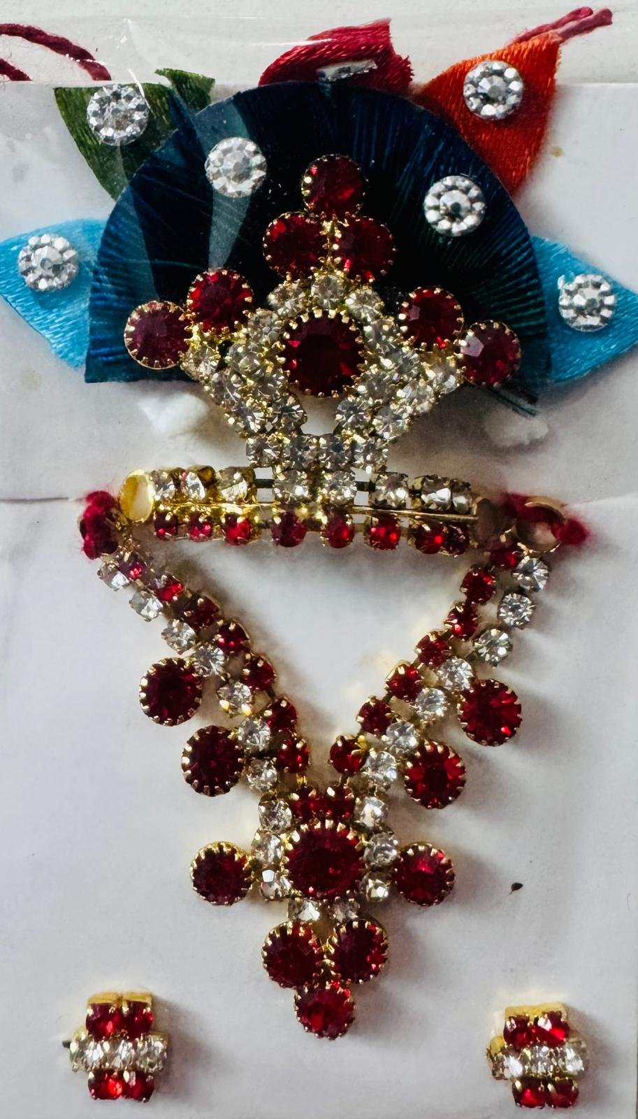 Laddu Gopal mukut and mala set with peacock-colored satin petals, ruby red stones, and white crystal highlights