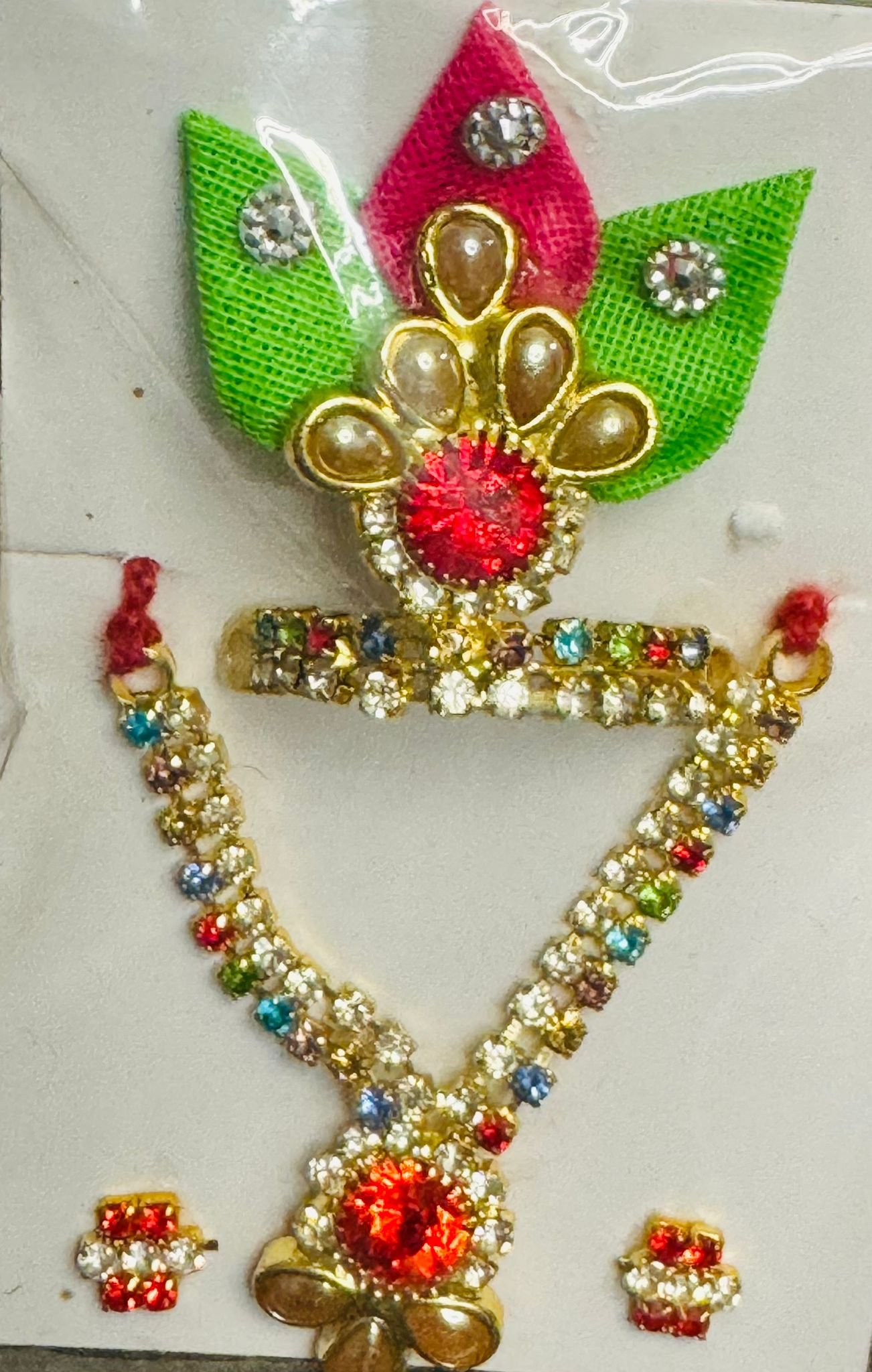Laddu Gopal mukut and mala combo with red centerpiece, multicolored stones, and green-pink fabric leaf design