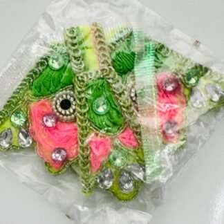 Green and pink floral embroidered dress corner patches for Radha Rani attire, decorated with silver stones and mirror work, packaged in a clear plastic wrapper.