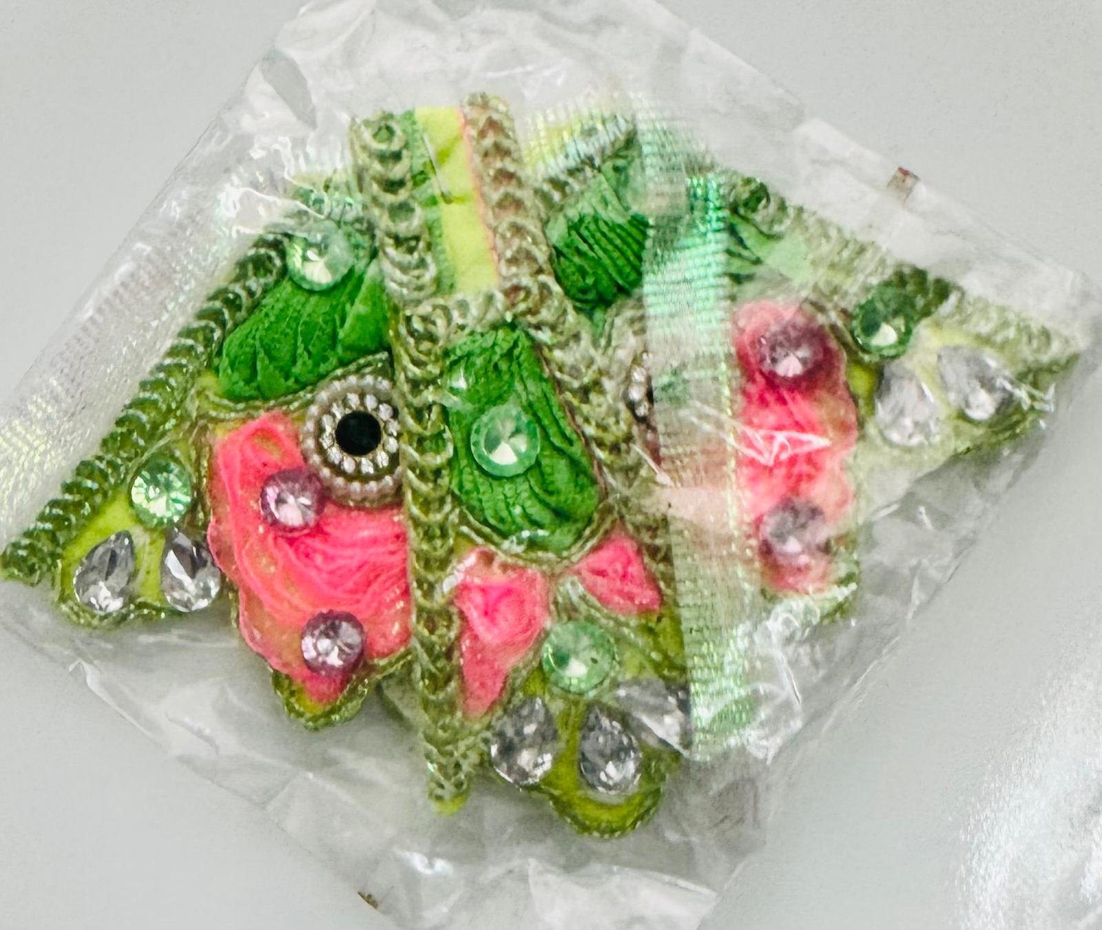 Green and pink floral embroidered dress corner patches for Radha Rani attire, decorated with silver stones and mirror work, packaged in a clear plastic wrapper.