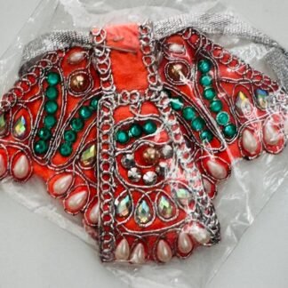 Orange Radha Rani dress with green and white gemstone detailing, silver lace accents, and tear-shaped embellishments, packed in clear plastic.