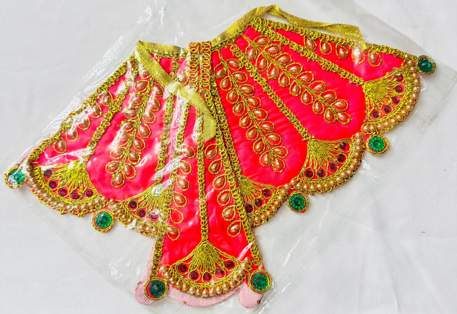 Peach Radha Rani dress with golden embroidery, pearls, and green gemstone accents